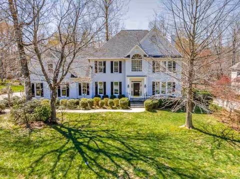 A large white two-story building with a manicured front yard and bare trees.