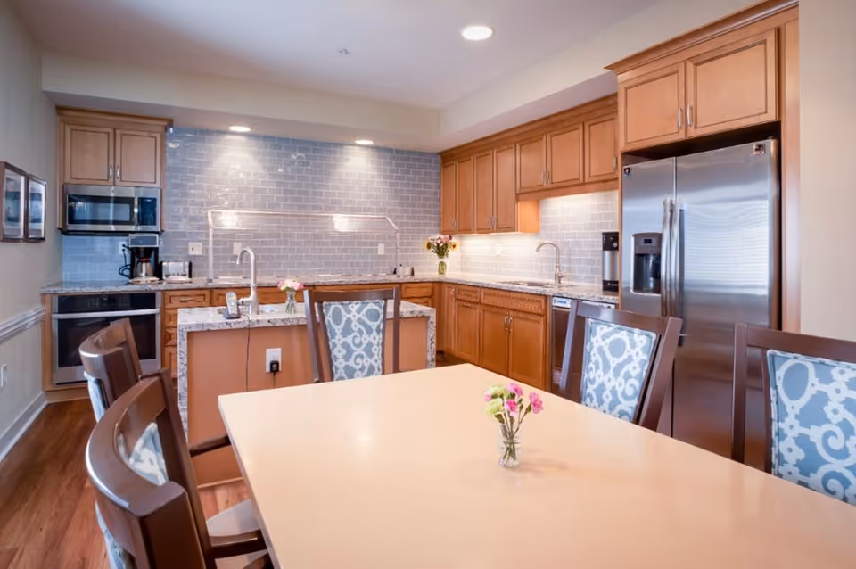 Open-concept kitchen and dining area with wooden cabinets, stainless-steel appliances, a center island, and a table with patterned chairs.
