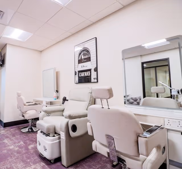 Salon-style interior with cushioned pedicure chairs, mirrors, and framed wall art in a softly lit room.