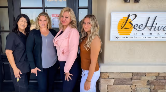 Four staff members stand smiling outside the facility entrance next to a BeeHive Homes sign.