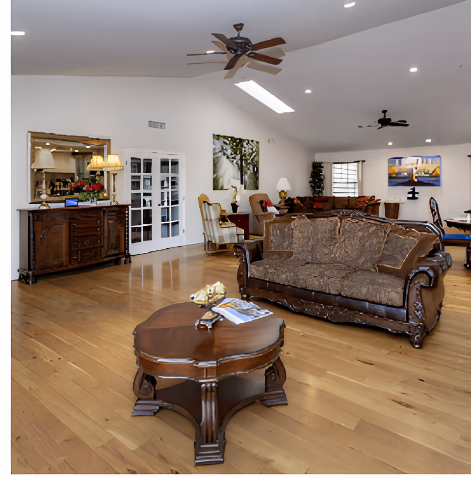 Large airy living room with hardwood floors, upholstered sofas, a central wooden coffee table, and ceiling fans.