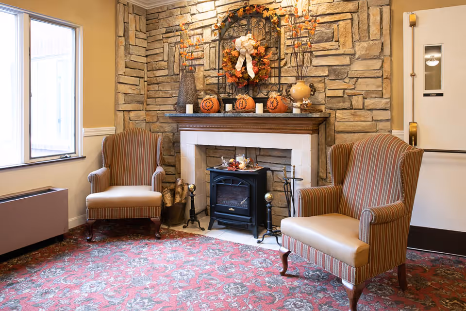 Cozy sitting area with two striped armchairs flanking a decorative stone fireplace topped with autumn decor and pumpkins.