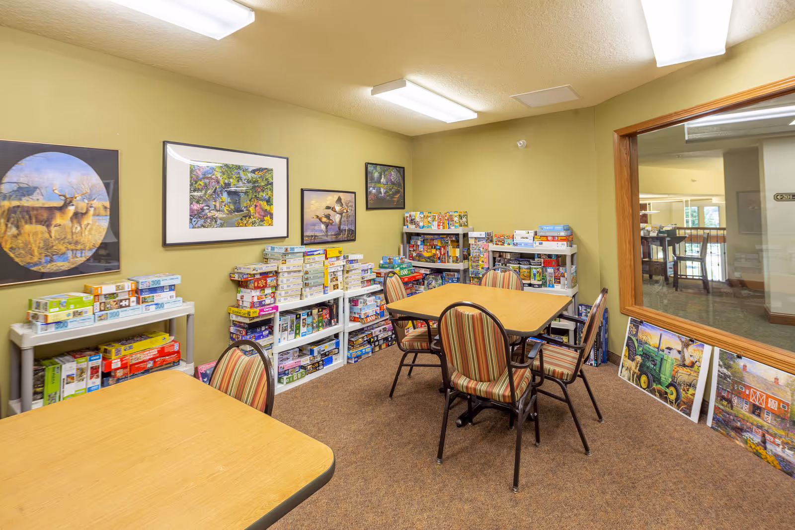 Small activity room with tables, striped chairs and shelves filled with board games and puzzles.