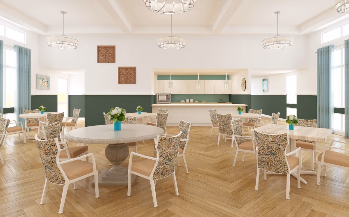 Bright communal dining room with round and rectangular tables, patterned chairs, wood herringbone floors, and a serving counter in the back.