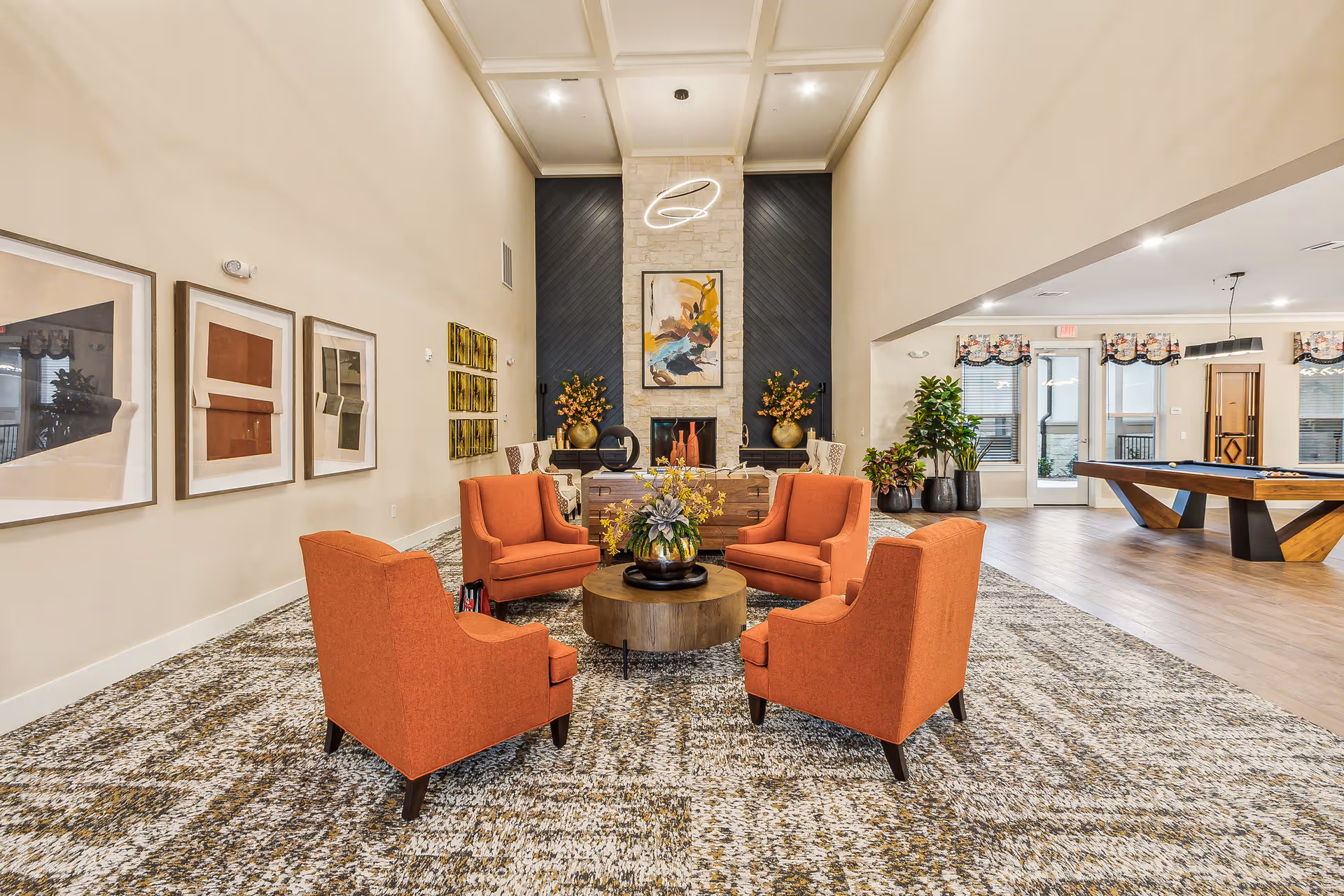 Bright communal lounge with four orange armchairs arranged around a round coffee table in front of a fireplace and artwork.