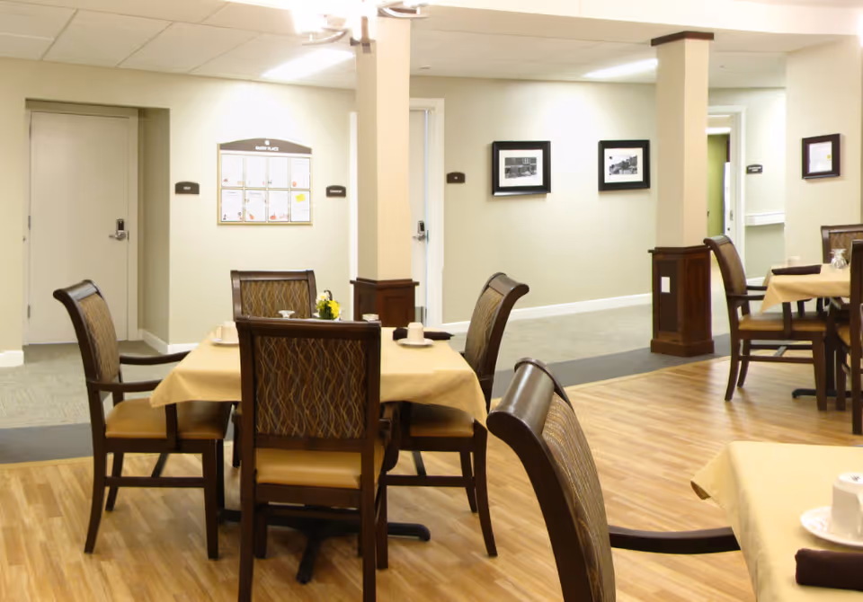 Indoor dining area with tables and chairs set with place settings in a senior living facility.