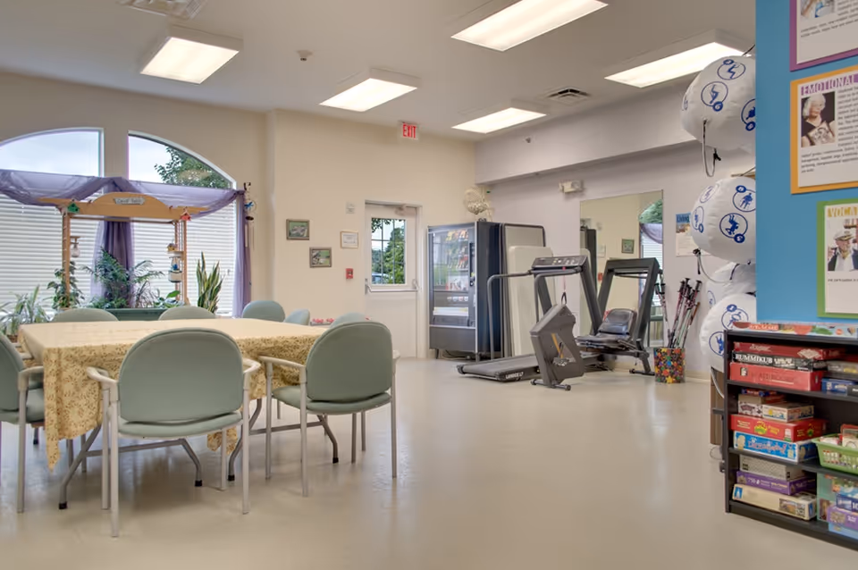 Interior common room with a table and chairs, exercise equipment, a vending machine, and a shelf of games.