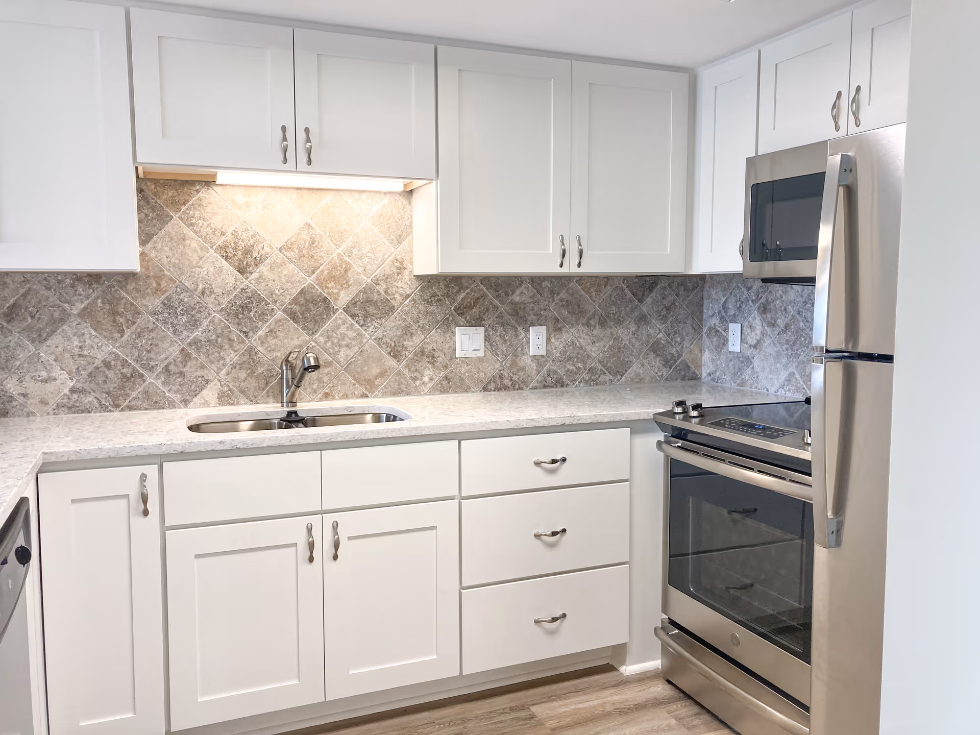 Bright modern kitchen with white cabinets, stone-tile backsplash, stainless steel stove and refrigerator, and a single-basin sink.