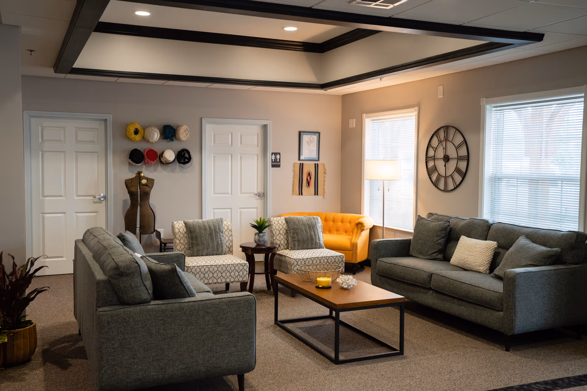 Comfortable common living room with sofas, armchairs, a coffee table, a yellow accent chair, and decorative wall accents.