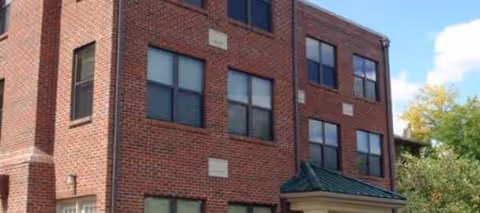 Brick three-story senior housing building exterior with windows and a small entrance canopy.