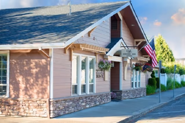 Pink single-story senior living building with stone base, awning, and American flag