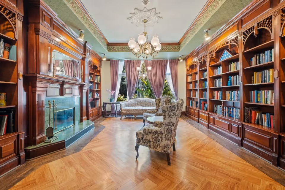 Elegant library-style communal lounge with built-in wood bookshelves, a fireplace, chandelier, and upholstered seating by draped windows.