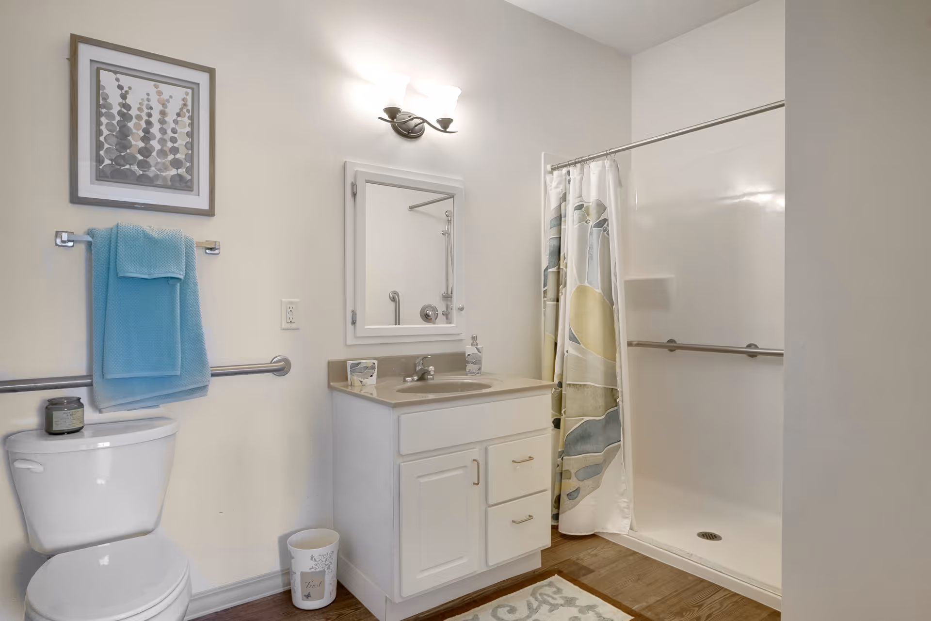 Well-lit bathroom with a toilet, vanity and sink with mirror, towel rack, and a walk-in shower with a patterned curtain.