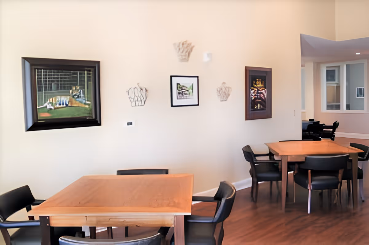 Dining area with wooden tables and black chairs against a beige wall decorated with framed artwork.