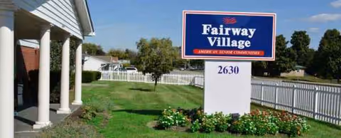 Exterior view of Fairway Village with sign, columns, white fence, and a well-kept lawn.