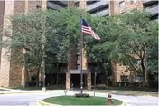 Brick apartment building entrance with flagpole, trees, and circular driveway in front.