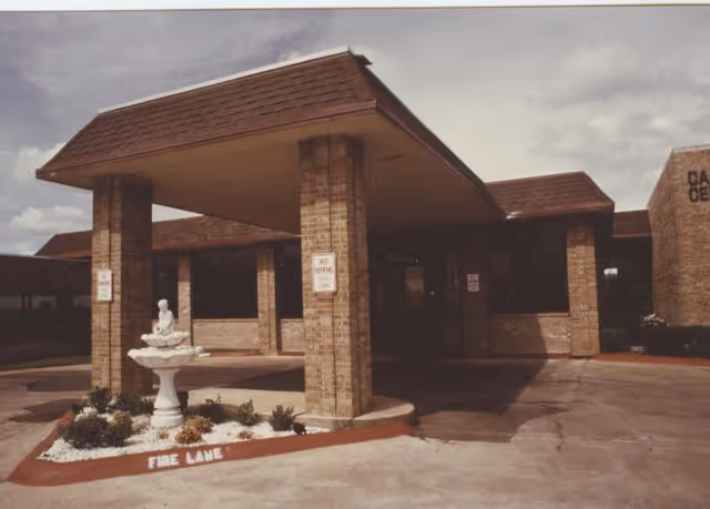 Covered brick entrance and portico of a nursing facility with a small decorative fountain and a painted 'FIRE LANE' curb.