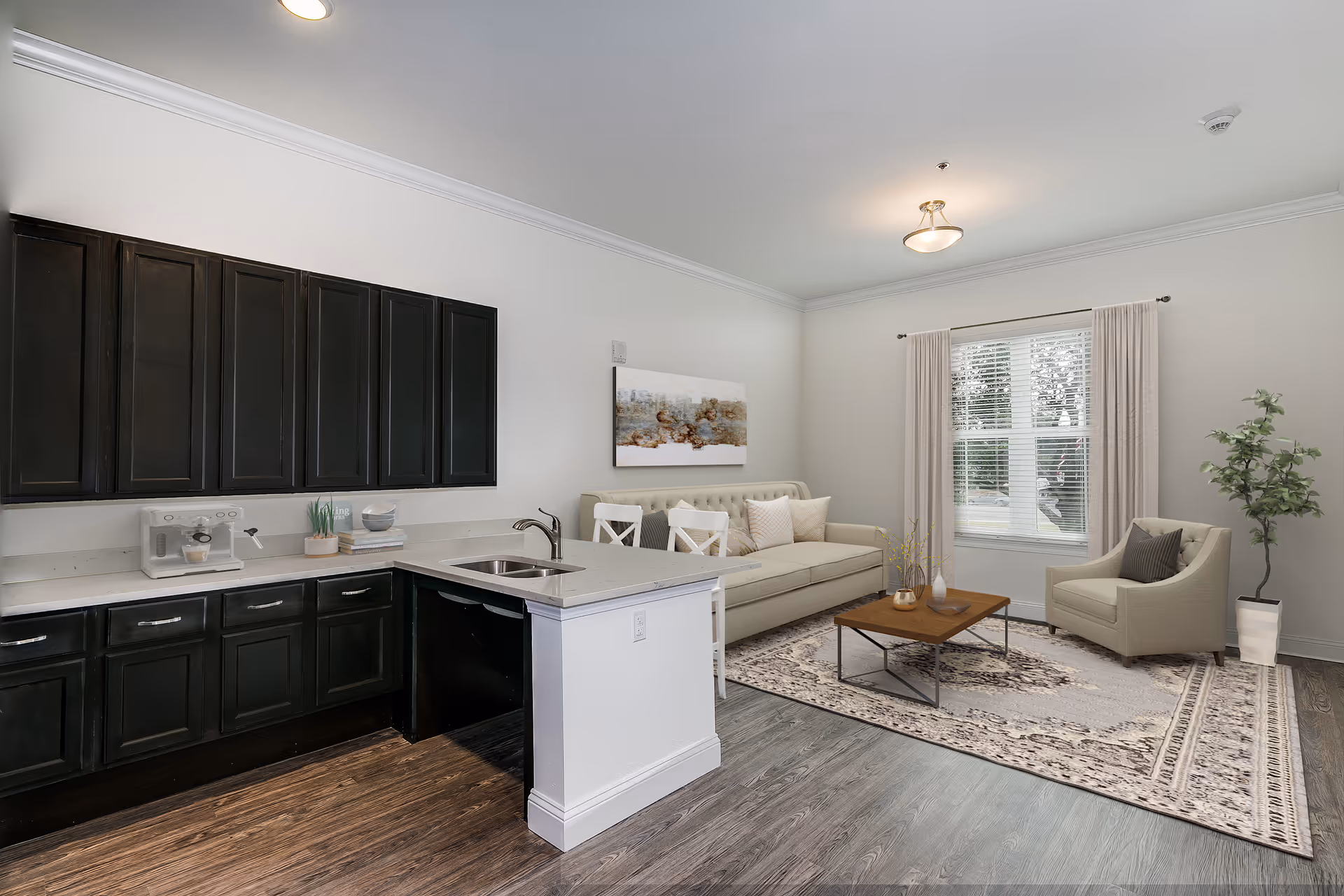 Open-plan living room and kitchenette featuring dark cabinets and a white island, a sofa and armchair on a patterned rug beneath a window.