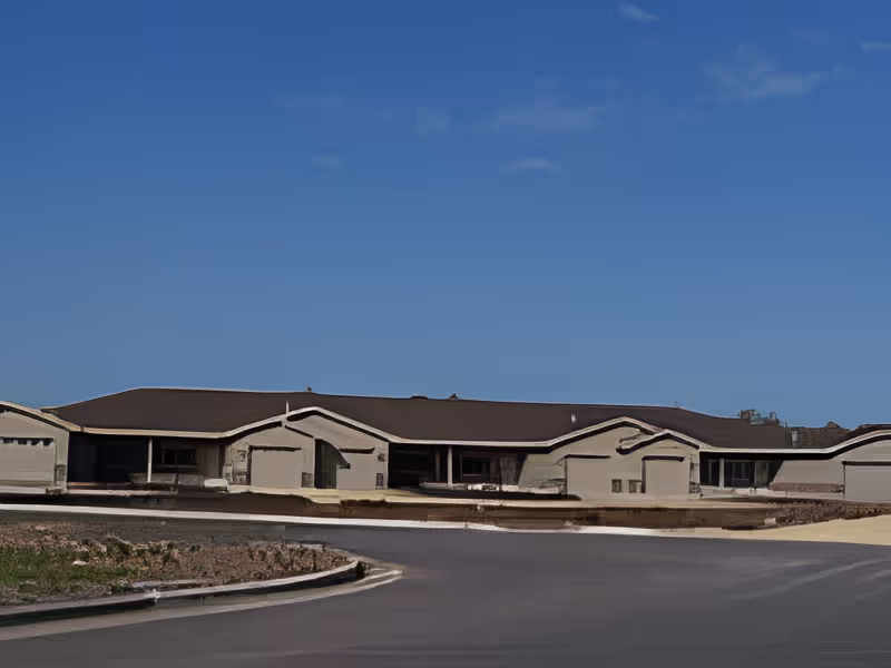 Exterior view of a single-story building with multiple garage doors under a clear blue sky.