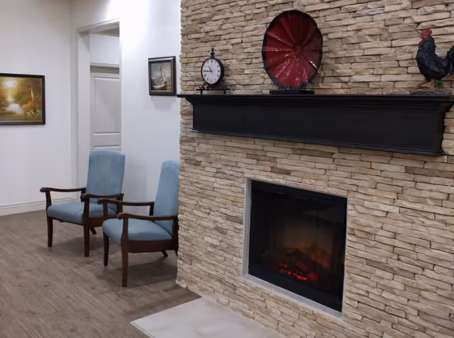 Two light-blue armchairs sit beside a stone fireplace with a black mantel displaying decorative items in a communal living area.