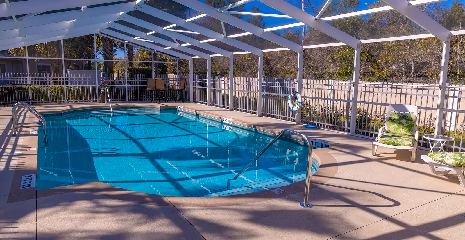 Screened outdoor swimming pool with metal handrails, lounge chairs, a life ring, and a white pergola-style enclosure.