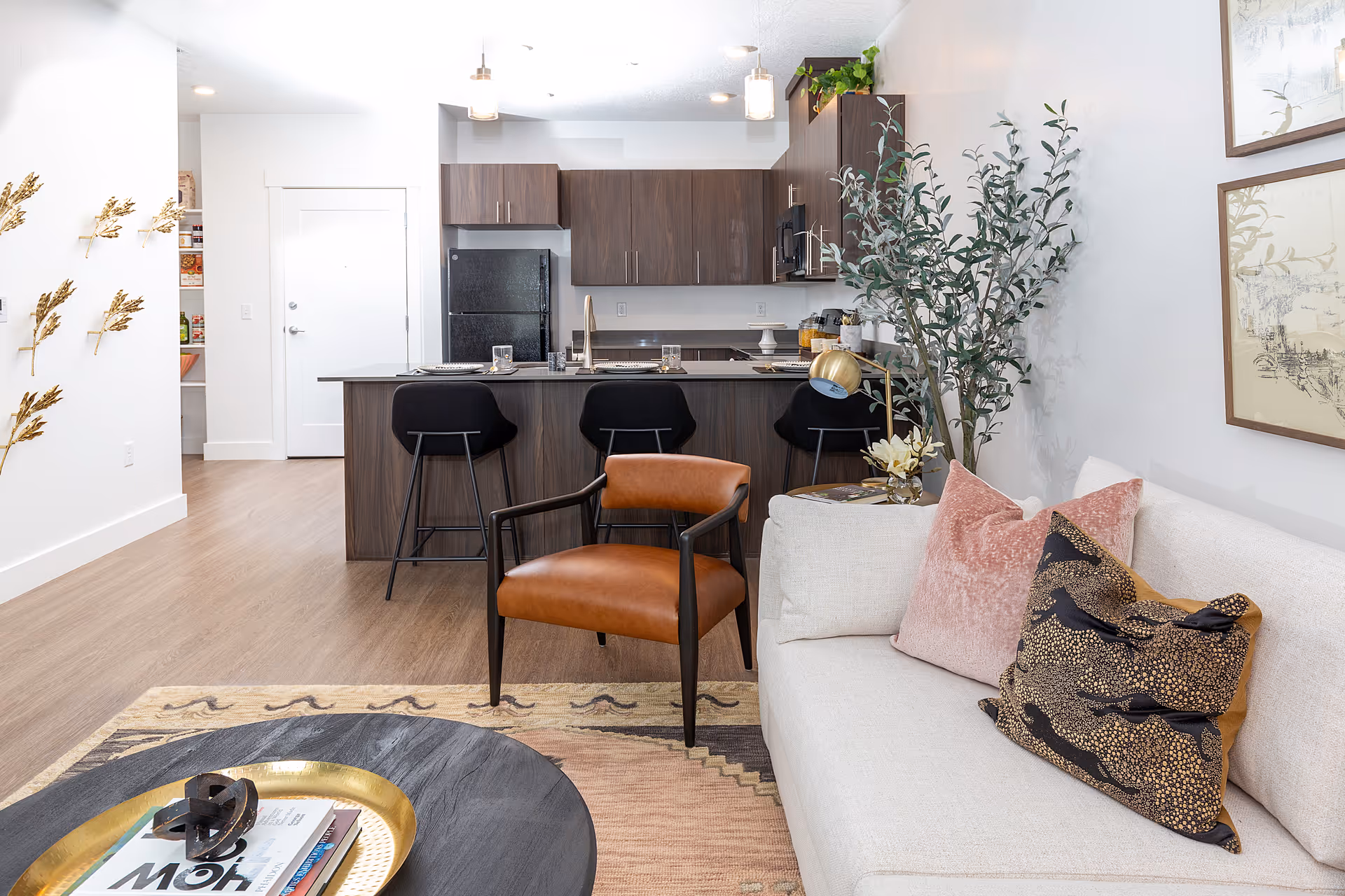 Open-plan living room and kitchen with a sofa, armchair, coffee table, and a kitchen island with bar stools.