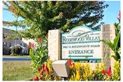 Entrance sign reading 'Rosewood Villas' surrounded by flowers and landscaping with the building and trees in the background.