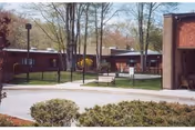 Exterior view of The Friendly Home Inc with brick buildings, trees, and a lawn.