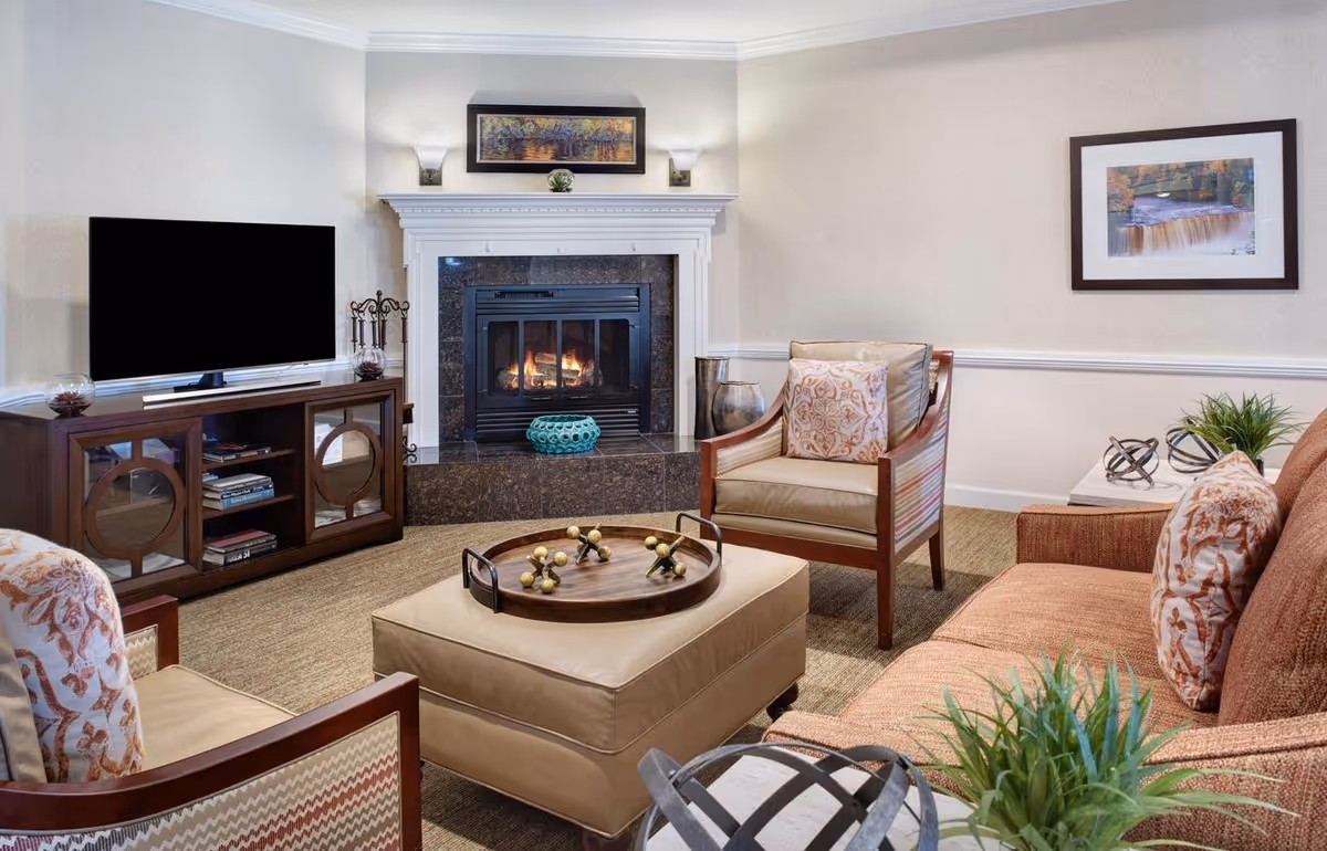 Comfortable living room with sofa, armchairs, ottoman, TV, and a lit fireplace.