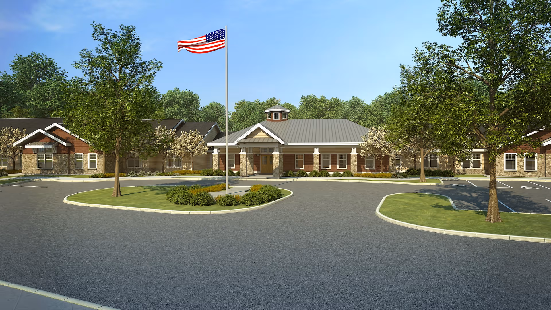 Front exterior view of a senior living facility with a circular driveway, landscaped greenery, several trees, and an American flag on a flagpole in the center. The building has a combination of brick and stone facade with a gray metal roof under a clear blue sky.