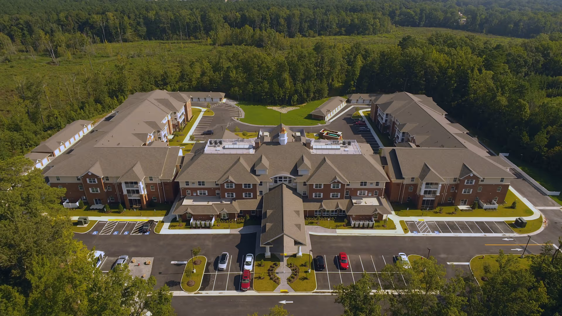 Aerial view of a large multi-wing retirement community building with parking lots and surrounding trees.