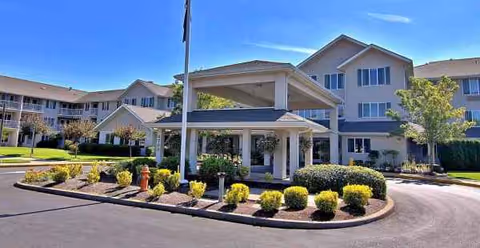 Exterior view of a senior living facility with a covered entrance and landscaping.