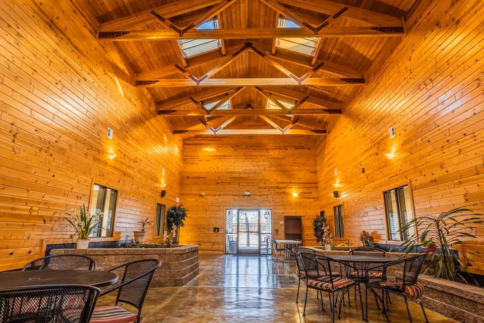 Large wood-paneled communal room with high beamed ceiling, skylights, and tables with chairs.
