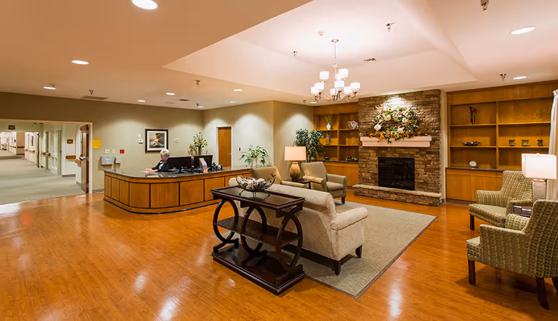 A warm reception lounge with sofas, a fireplace, and a front desk with a staff member.