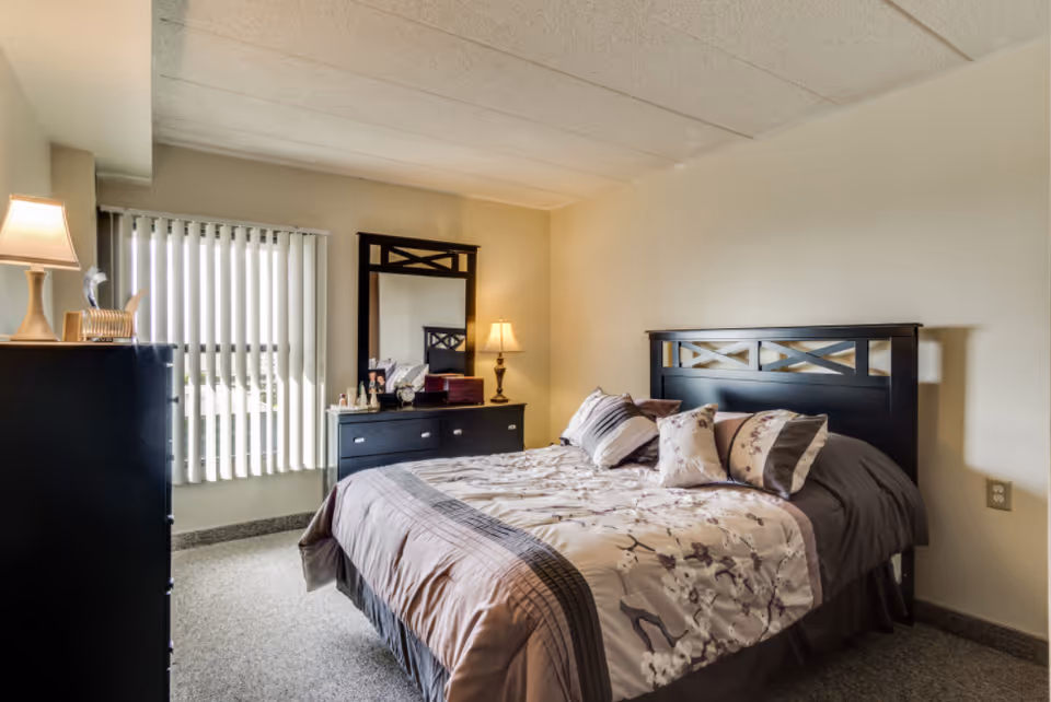 Bedroom with a dark wood bed, dresser, mirror, and neutral decor.