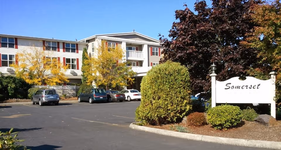 Front exterior of a multi-story senior living building with parked cars, landscaping, and a sign reading 'Somerset'.