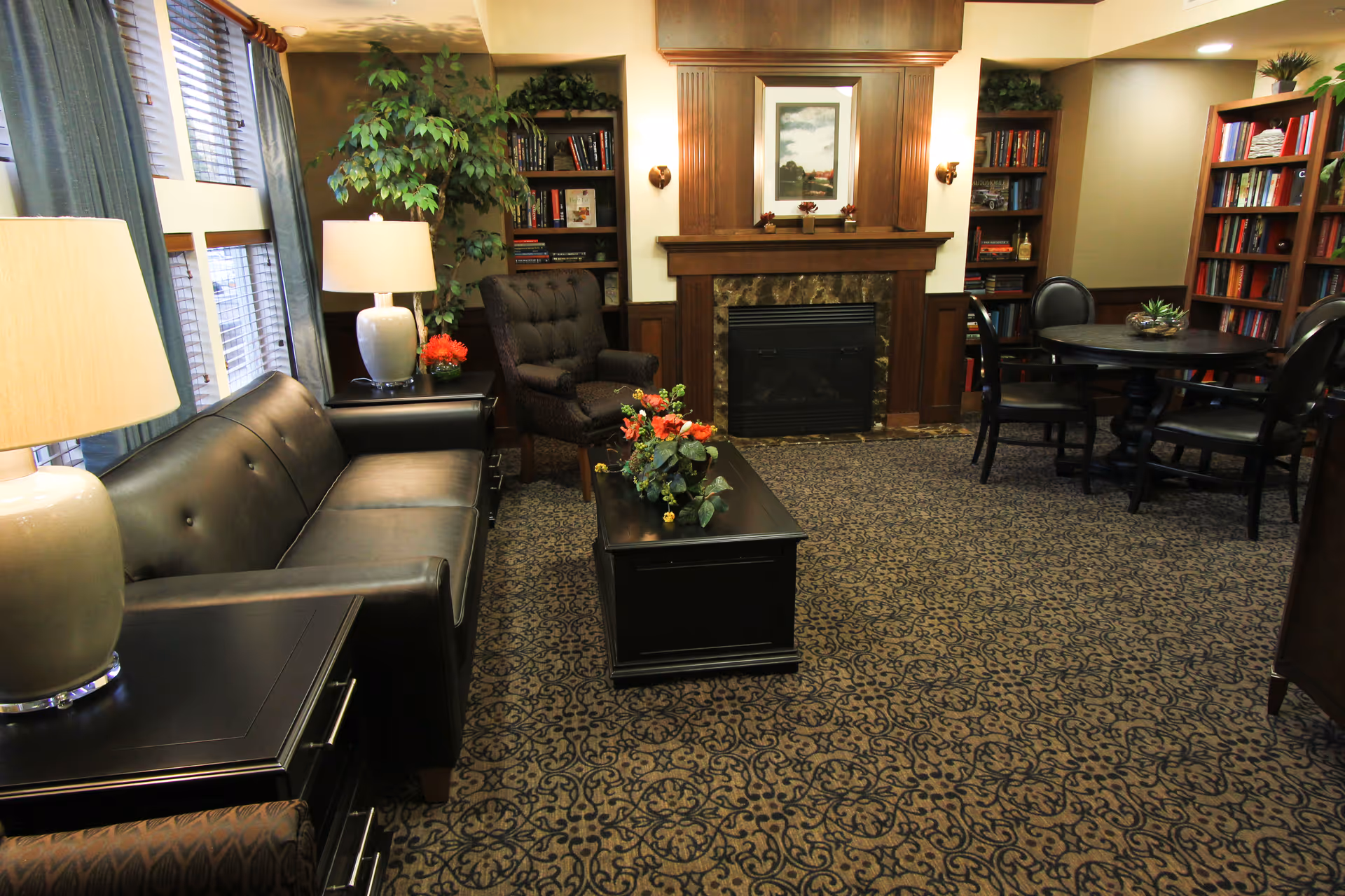 Comfortable common room with a leather sofa, armchair, coffee table, fireplace and bookshelves.