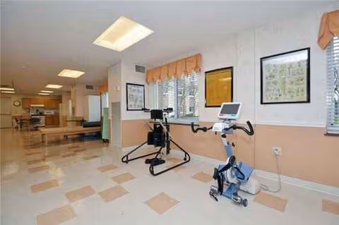 Indoor rehabilitation gym with exercise bikes, therapy equipment, peach walls, and framed pictures.