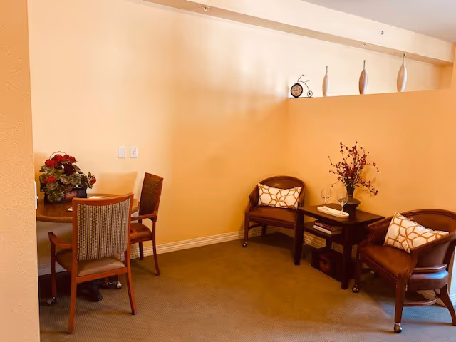 Small interior seating area with chairs, side tables, decorative cushions, flowers and vases on a shelf.