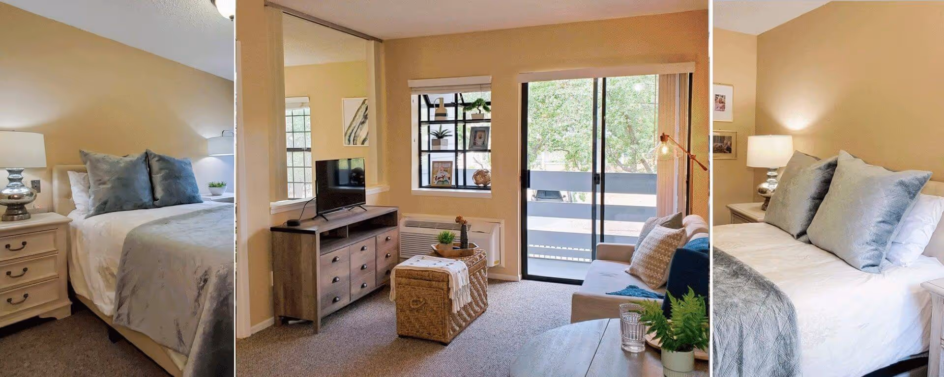 A senior living facility interior featuring a cozy bedroom with a bed, bedside tables, and lamps on each side, decorated with blue pillows and a gray blanket. Adjacent to the bedroom is a living room area with a TV on a wooden dresser, a wicker ottoman, a sofa with cushions, a floor lamp, and a sliding glass door leading to a balcony with greenery outside.