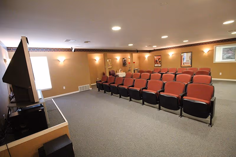 Small auditorium-style interior with rows of red theater seats facing a large screen/TV.