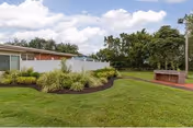 Grassy courtyard with landscaped planting beds, a brick outdoor grill or fireplace, and a low single-story building under a partly cloudy sky.