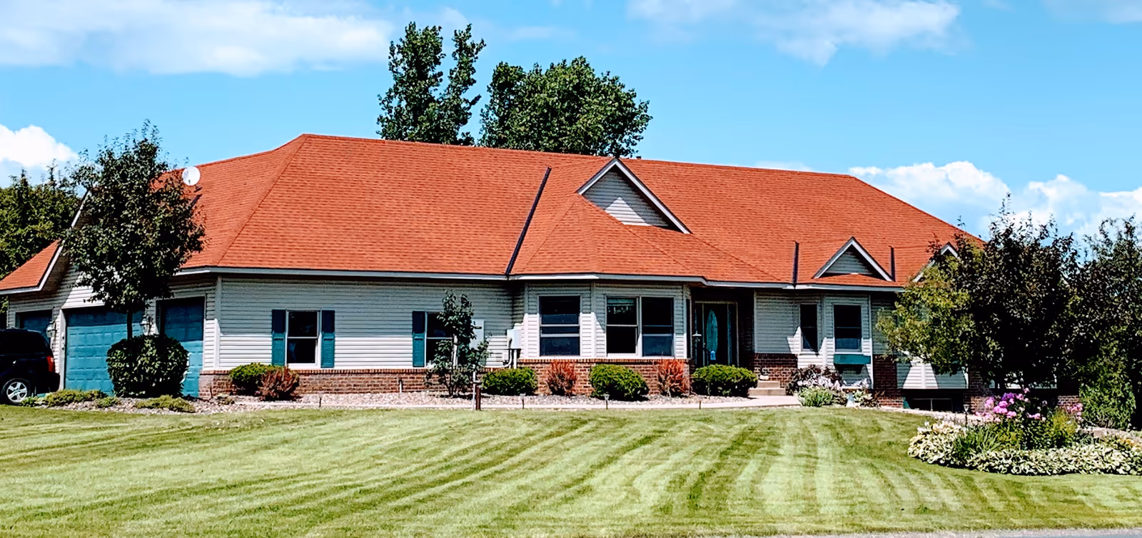 Single-story assisted-living style house with a red roof, light siding, green shutters, attached garage and a manicured front lawn under a blue sky.