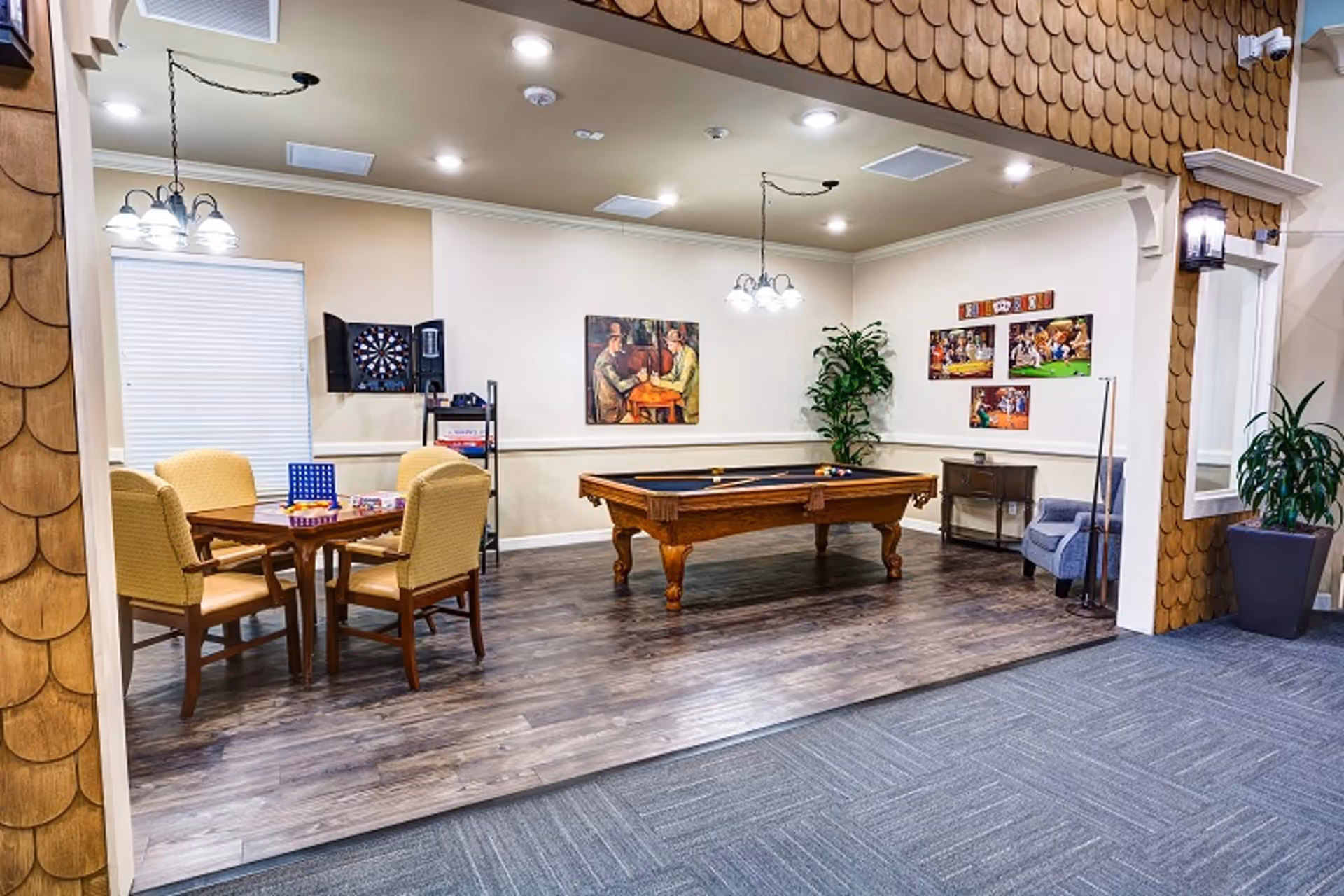 Open recreation room with a pool table, card table and chairs, dartboard, and wall artwork.