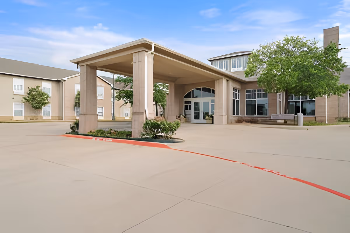 Covered porte-cochere and driveway leading to the front entrance of a multi-story senior living building.
