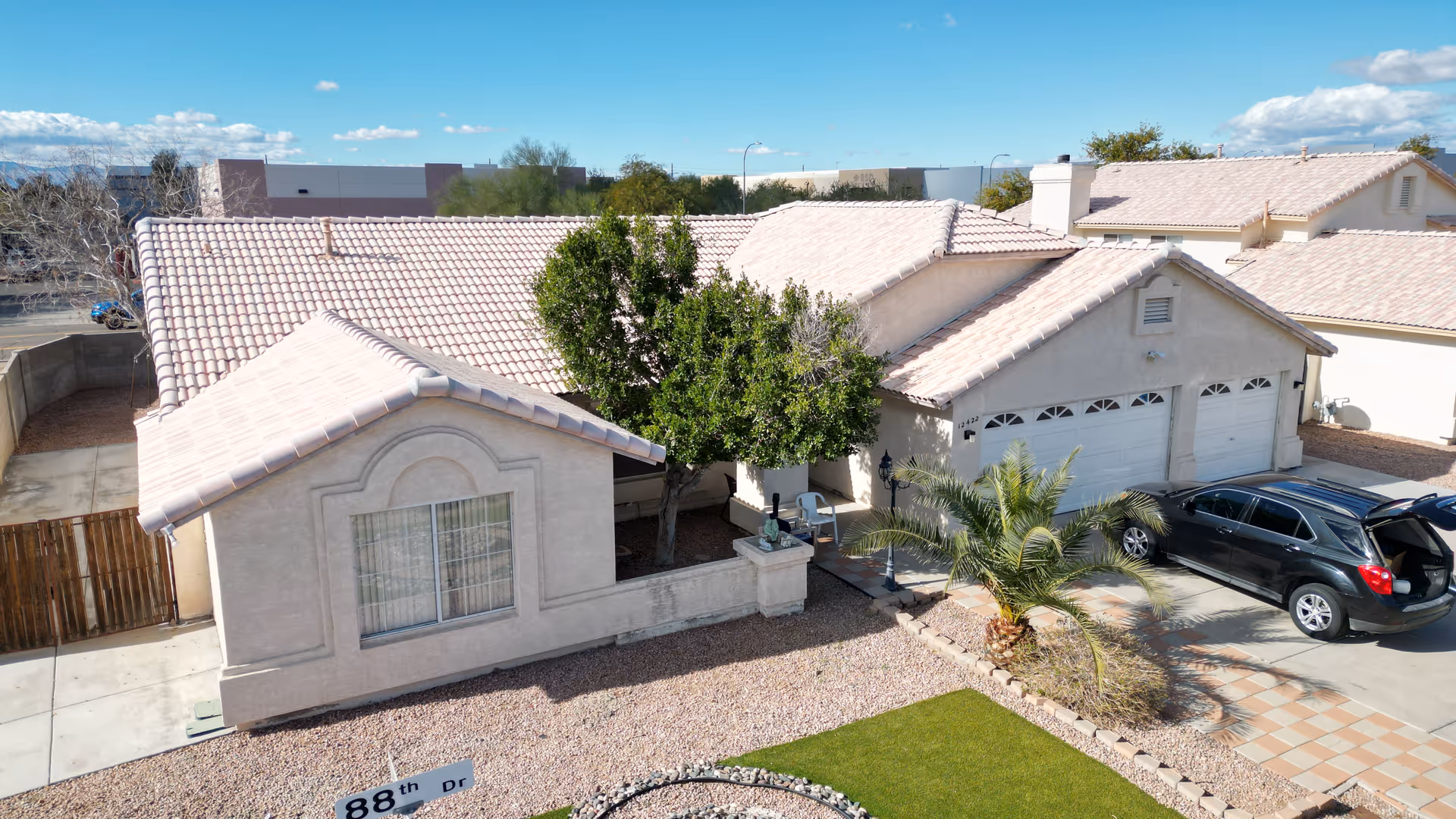 Front exterior of a single-story stucco house with a tiled roof, front yard, driveway, garage, and a parked car.