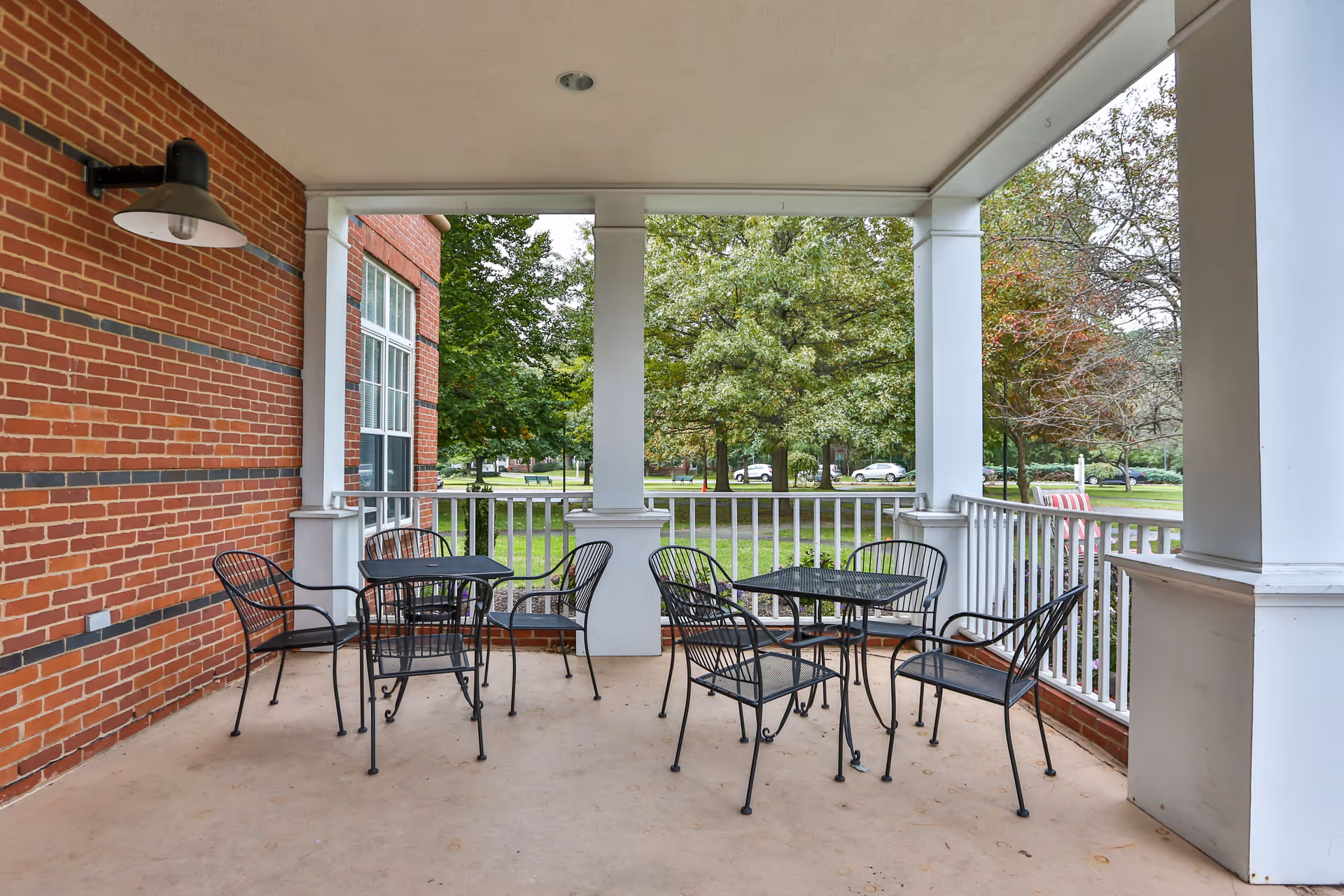 Covered outdoor patio on a brick building with metal tables and chairs overlooking a tree-lined street.
