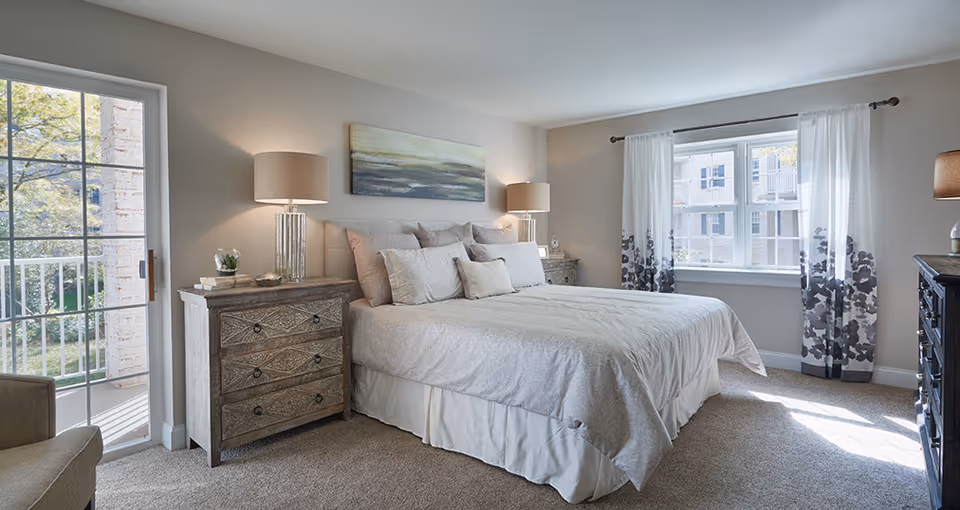 Bright, neatly staged bedroom with a large bed, matching nightstands and lamps, and windows letting in natural light.