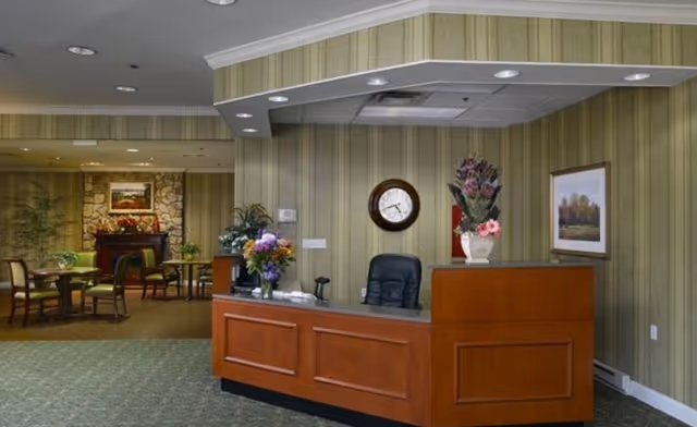 Lobby reception area with a wooden front desk, floral arrangements, wall clock, and a seating area with tables and chairs.