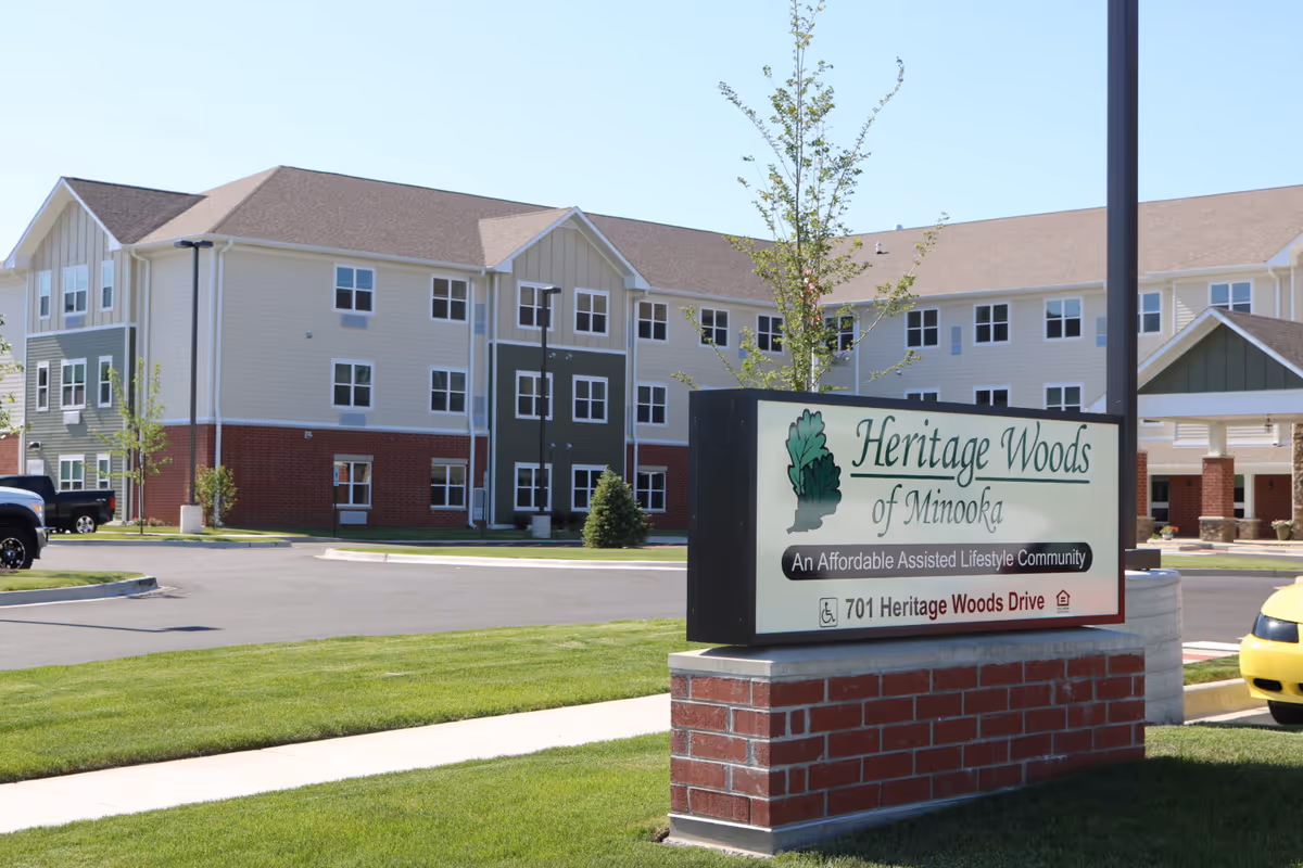 Exterior front view of the Heritage Woods of Minooka assisted living building with a large sign by the driveway.